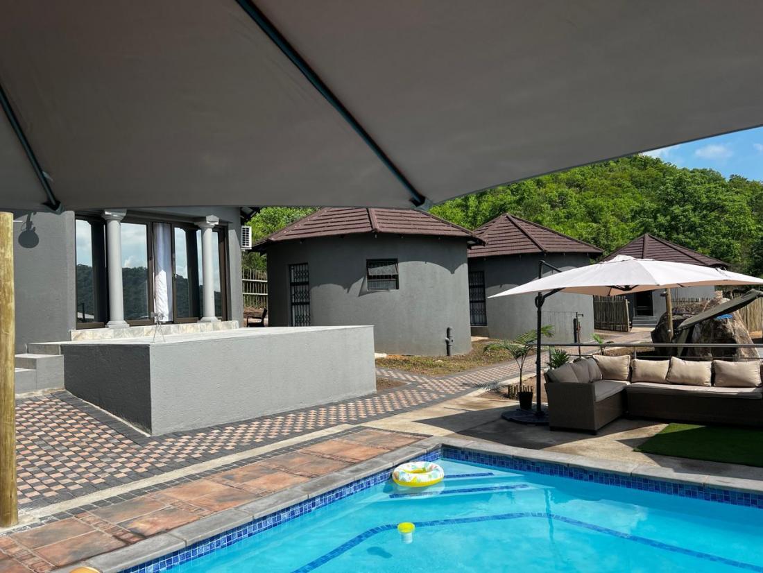 Pool with umbrella and chalets viewed from the shaded lodge terrace