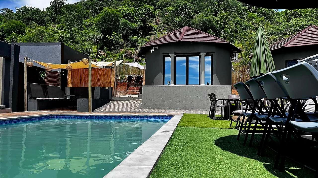 Swimming pool and shaded lounge deck at Matjulu Kruger Lodge with green hillside behind